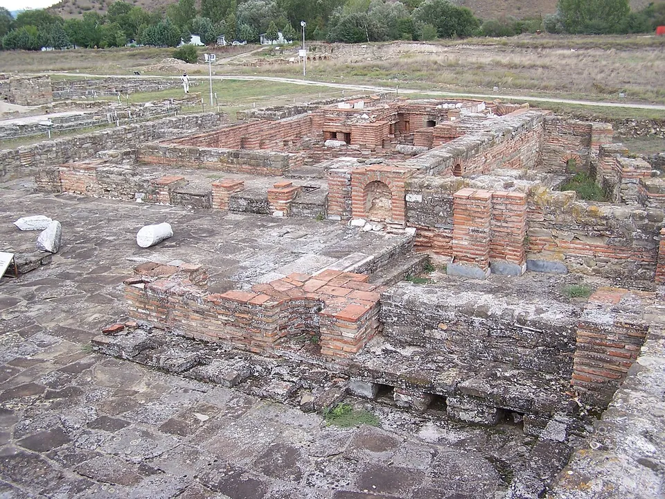 The walls of a bath building in courses of stone and red brick, with small brick arches and square brick piers standing on a stone-paved floor.