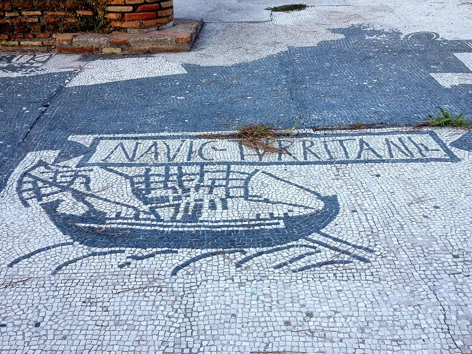 A black-and-white floor mosaic of a ship with oars and a steering oar, under a framed inscription beginning NAVIC.