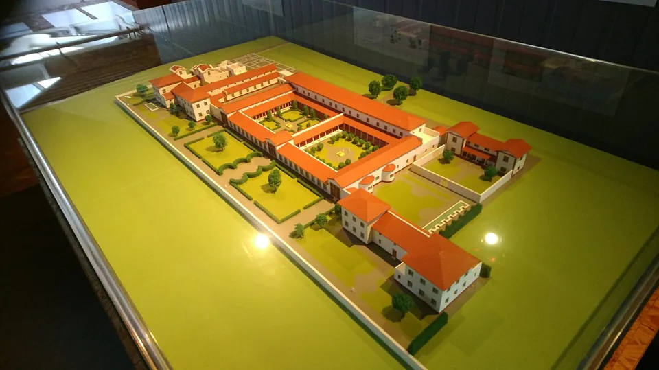A tabletop model under glass of a large villa, rows of buildings with red-tiled roofs set around several green courtyards and gardens.