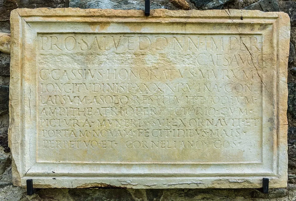 A large rectangular marble slab with a moulded frame, carved with several lines of Roman capital letters, set against a stone wall.