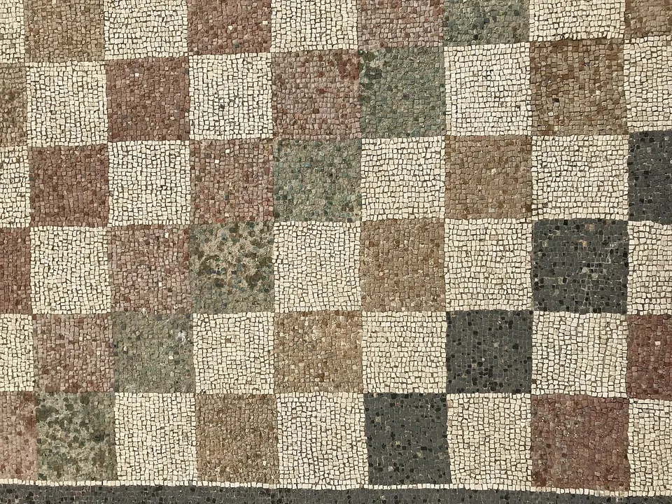 A close-up of a mosaic floor laid as a checkerboard of squares, white squares alternating with squares of pink, green, brown and black stone tesserae.