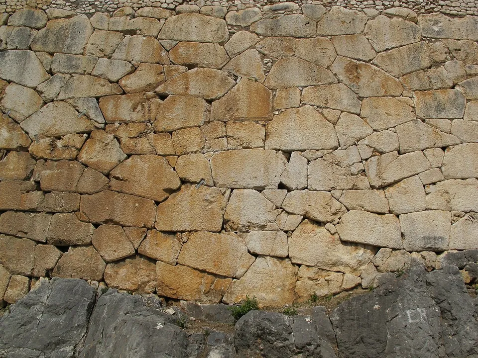 Close-up of a wall face of many-sided pale limestone blocks cut to fit one another, with a band of small rubble stones along the top.