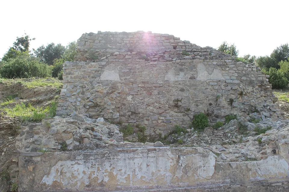 A rough rectangular block of mortared stone masonry standing on a low base, with grass and bushes around it.
