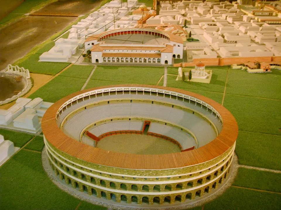 A white scale model of a walled Roman town seen from above, with a three-tiered oval amphitheatre in the foreground outside the wall and a semicircular theatre against the wall behind it.