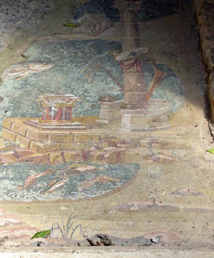 A worn floor mosaic in blues, greens and reds, with fish swimming in water around a small red structure and a column, its surface patched and broken in places.