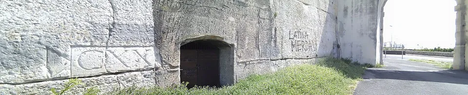 A sheer, smoothed rock face beside a road, with the numerals CXX carved in a framed panel on the left and a small arched doorway cut into the rock.