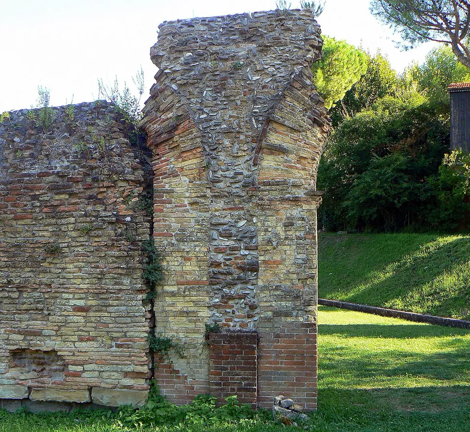 Close view of a pier built of courses of pale and red brick with a core of rounded stones set in mortar, the curve of an arch springing from its top.