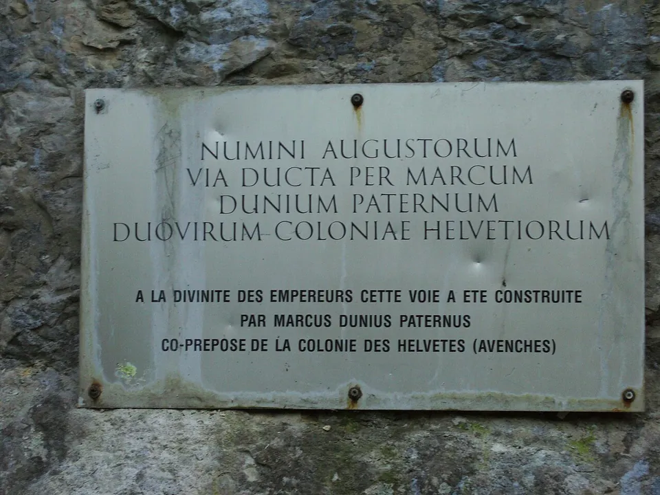 A metal plaque screwed to the rock giving the Latin text of the inscription in capitals, with a French translation below.
