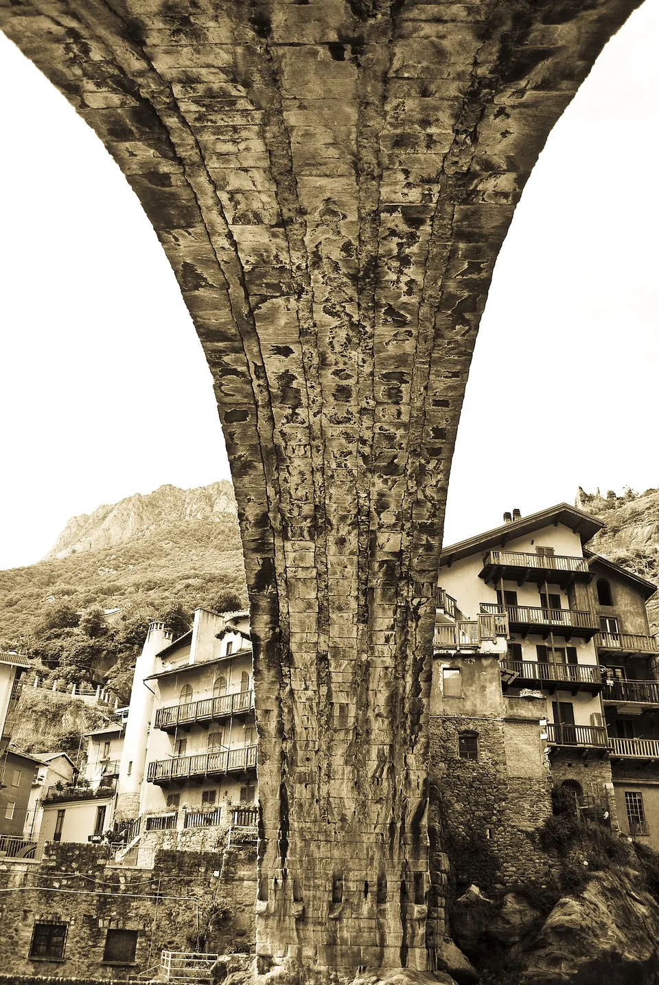 A sepia photograph looking straight up at the underside of the arch, its rough stone vault curving overhead between houses with wooden balconies.
