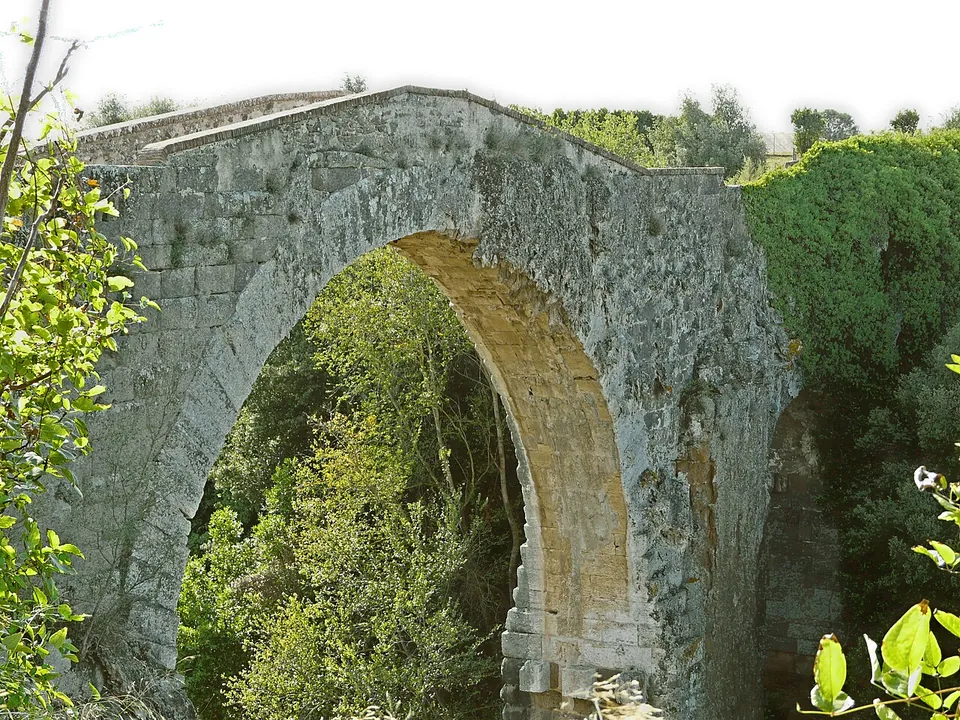 Close view of the arch, built of large squared grey and yellowish stone blocks, its curve framed by green foliage, with the edge of the deck along the top.