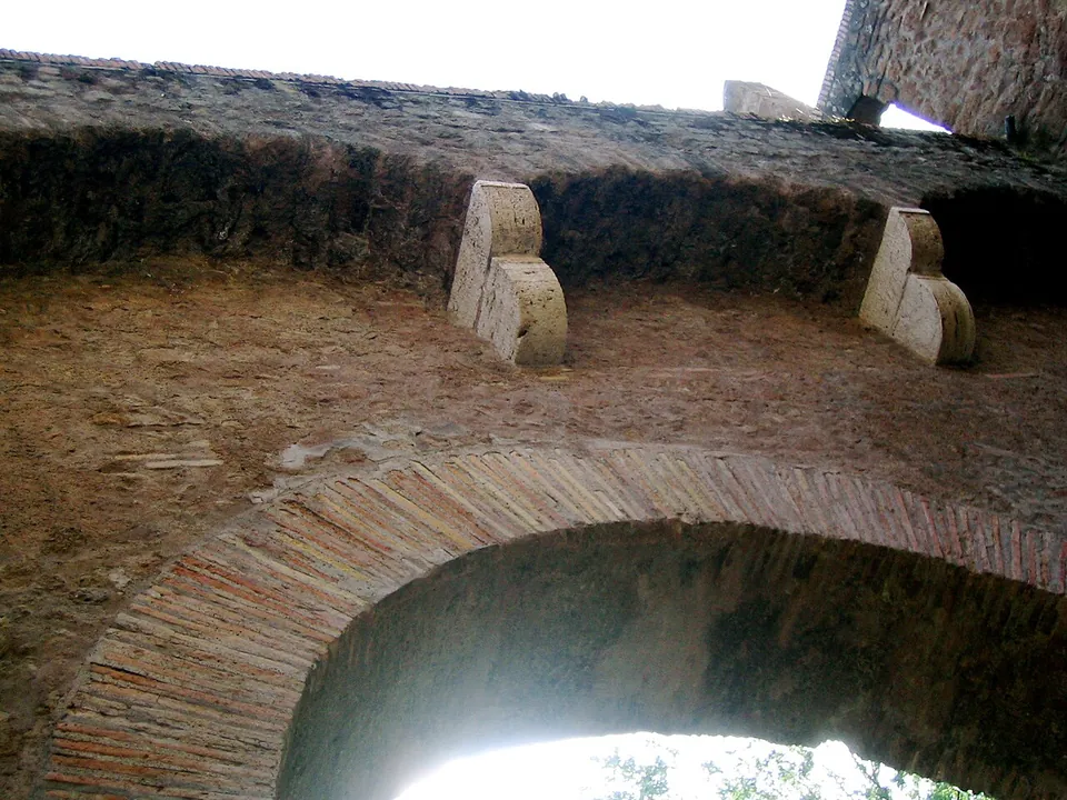 Looking up at a brick arch in sunlight, with two carved pale stone brackets projecting from the rough wall above it.
