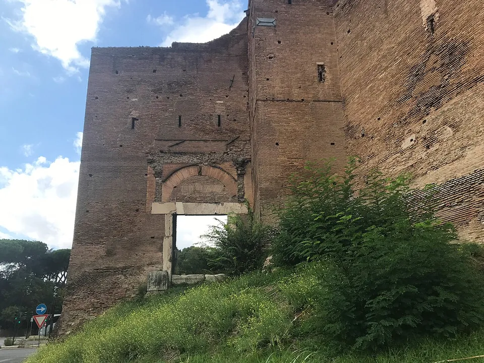 A tall brick wall rising from a grassy bank, with a small opening framed in pale stone and topped by a brick arch set low in it.