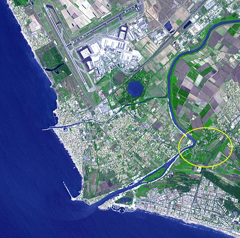 A satellite view of the coast west of Rome, with the runways and terminals of the airport at upper left, a dark six-sided lake just below them, the Tiber winding through fields on the right to the sea, and a yellow circle drawn around a bend of the river near the bottom.
