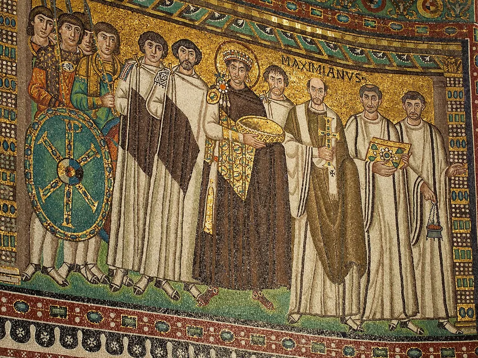A mosaic panel on a gold ground. At the centre a haloed, crowned man in a purple cloak holds a large golden bowl; to his left stand soldiers behind a shield bearing a Chi-Rho, to his right men in white robes and a man holding a jewelled cross, with the word MAXIMIANVS above his head.