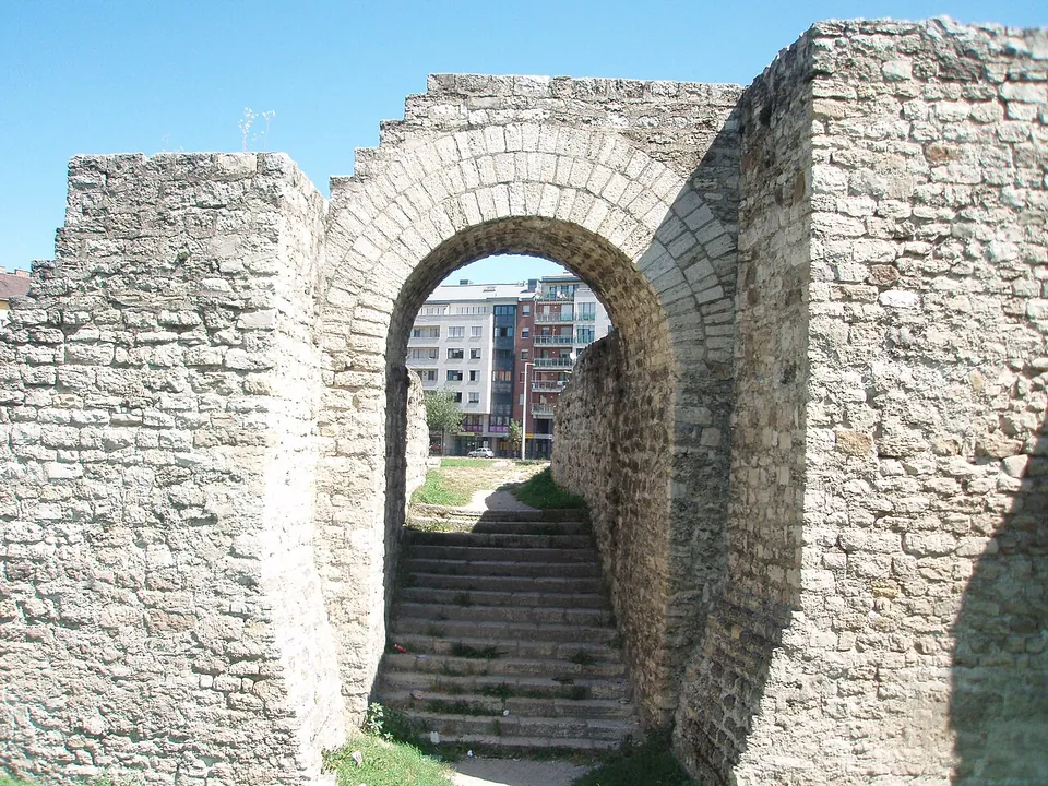 A round-headed vault of limestone blocks between two thick walls, with a flight of stone steps climbing through it towards modern buildings.