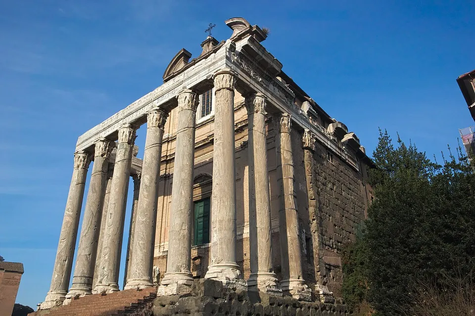 A temple portico of tall unfluted columns seen from below at a corner, with a later church facade and a green door set behind the columns.
