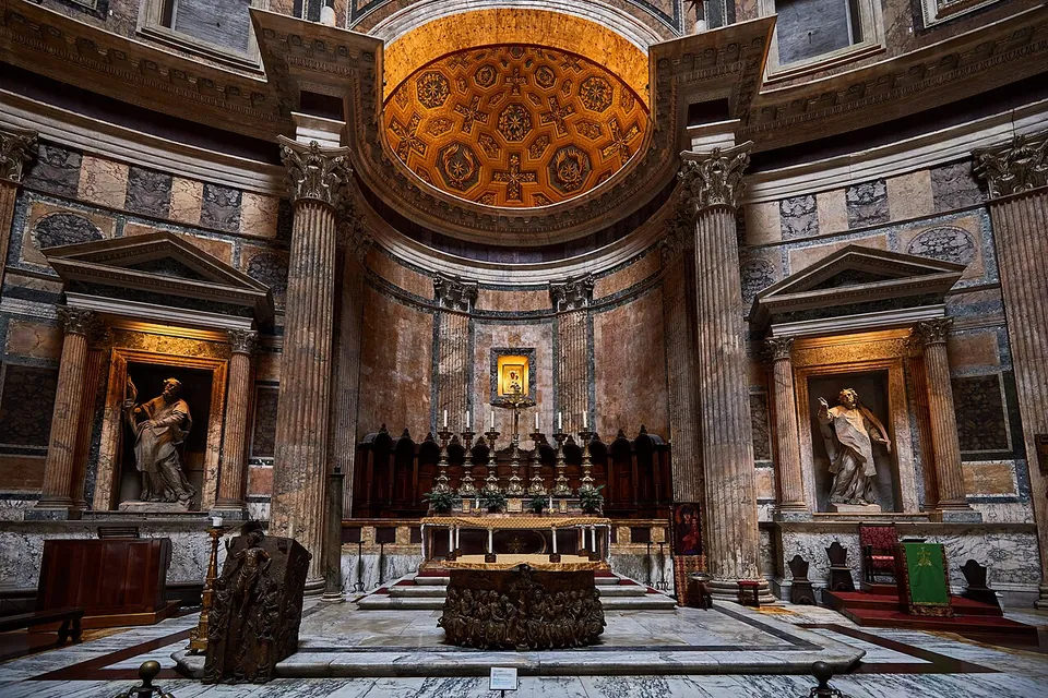 Inside the rotunda, a marble floor leading to the main altar in a deep apse with a gilded, coffered half-dome, flanked by fluted columns and niches holding marble statues.