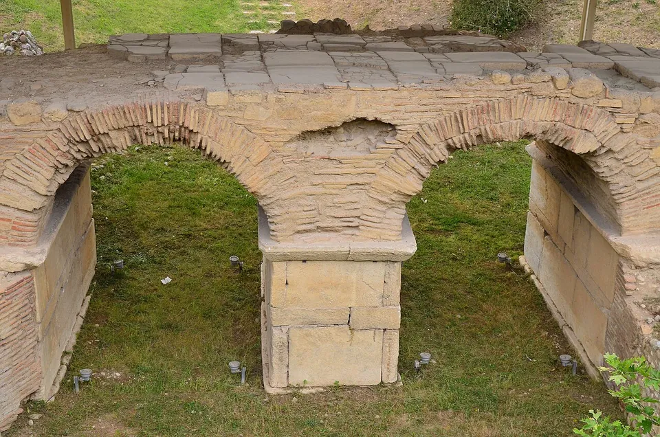 A low bridge of two brick arches on a squared stone pier, its deck of worn stone slabs, sunk in a grassy hollow with small lights in the ground.
