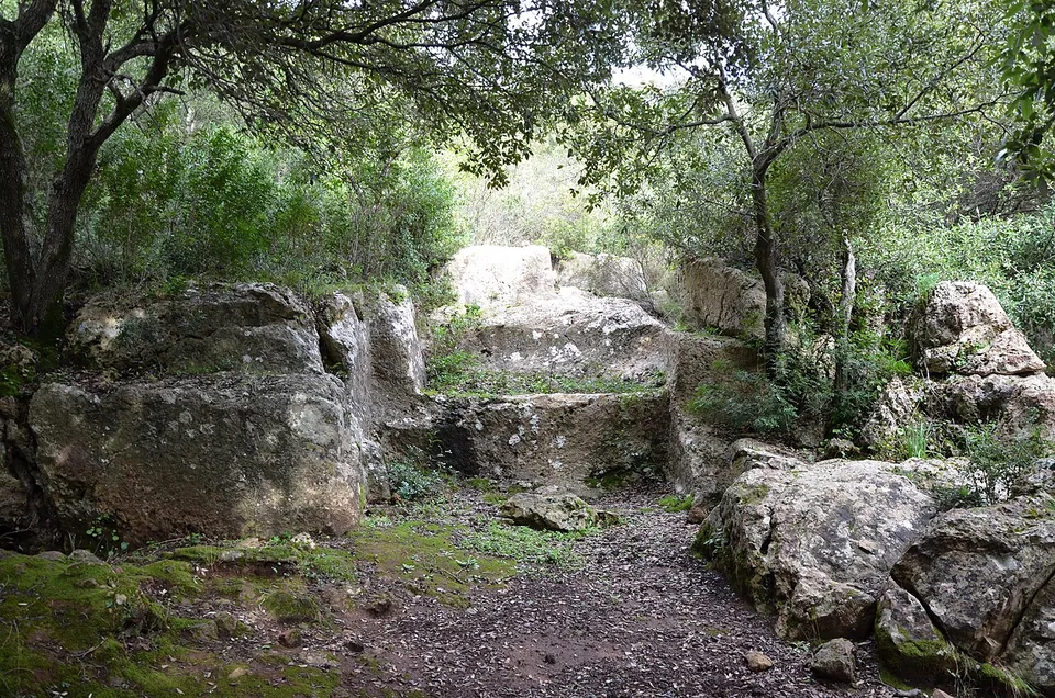 A path running between large pale limestone boulders and rock faces under trees, the stone partly covered in moss.
