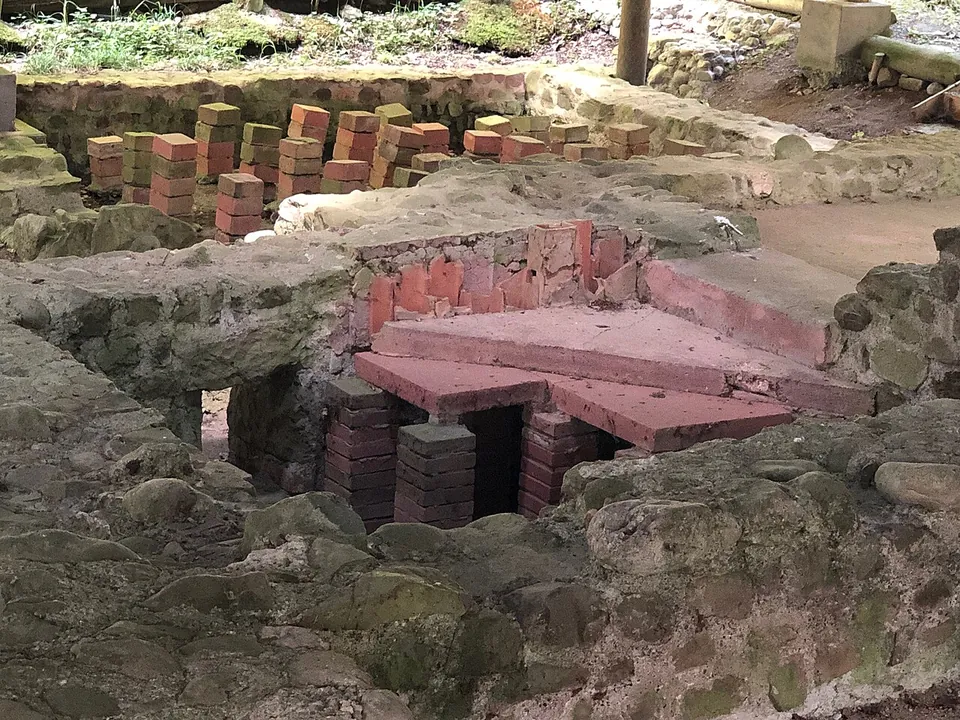 A close view of short stacks of square red bricks standing in a sunken room, some carrying large flat tiles, framed by rough stone walls.