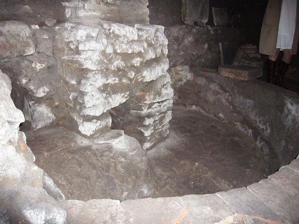 A round sunken basin edged with worn stone, with a rough block of masonry standing inside it.