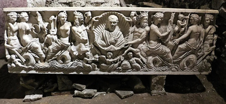 The long front of a marble sarcophagus carved in high relief with sea creatures and reclining figures riding on the waves, around a central portrait bust set in a scallop shell.