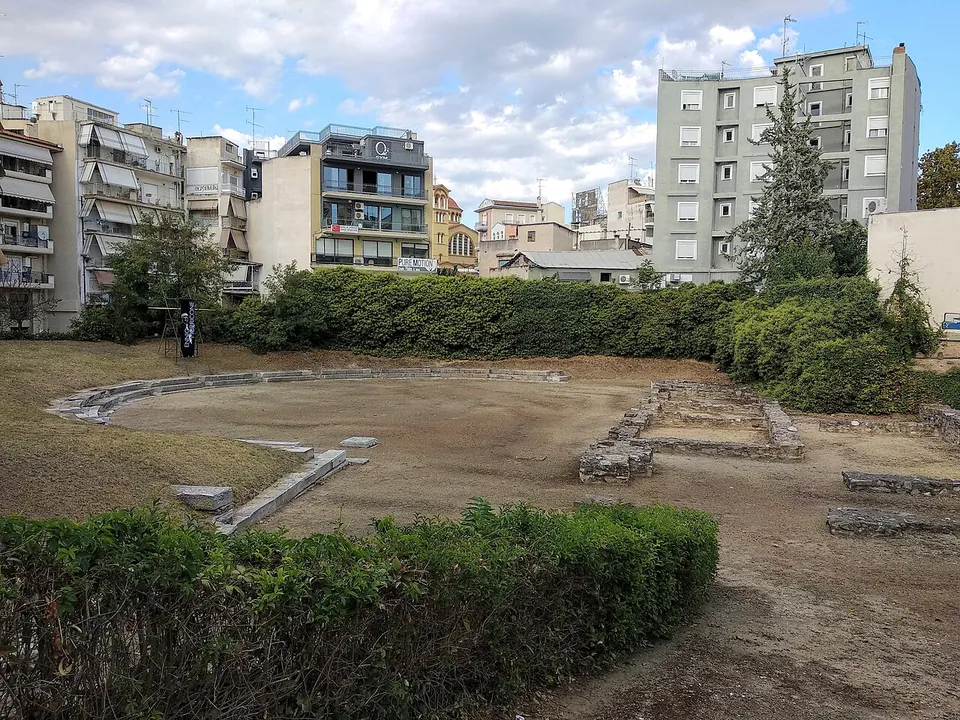A flat earth orchestra edged by a low curved kerb of stone, with low walls of the stage and hedges in front, among apartment blocks.