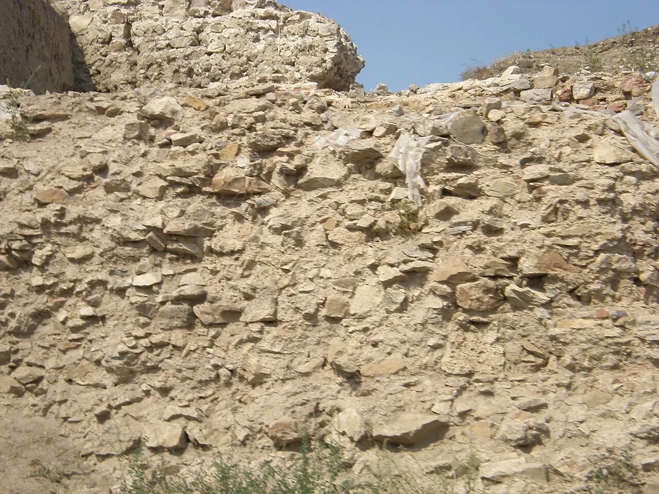 Close view of a wall face of rough, uneven stones set in mortar, its top ragged against the sky.