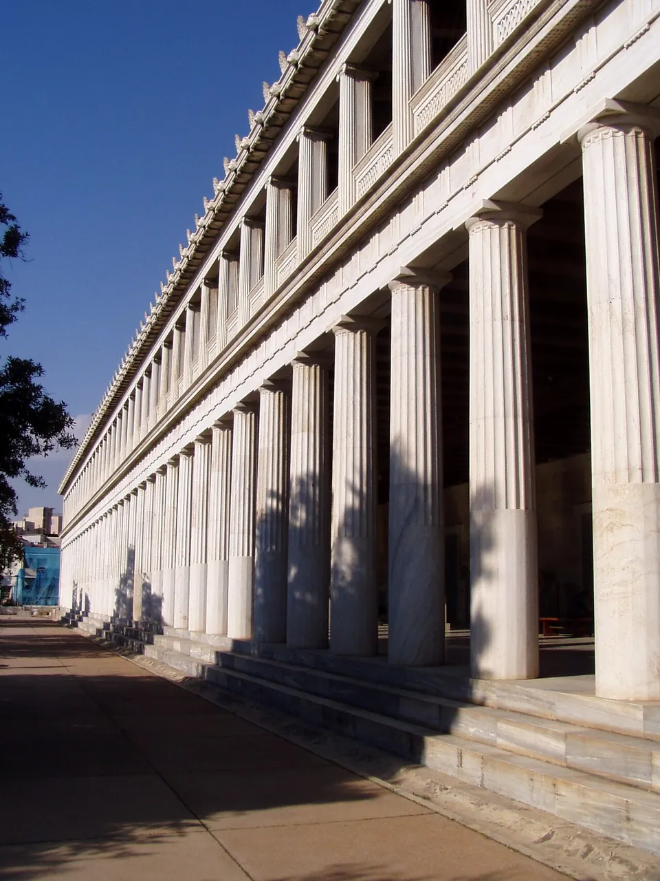 A long two-storey colonnade of white marble columns on a stepped base, seen along its length in bright sun.