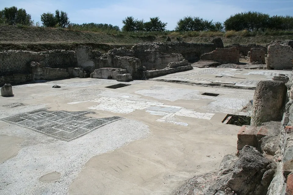Two rooms seen from above, each floored with a black-and-white mosaic of interlocking geometric and meander patterns, between low walls of rough stone.
