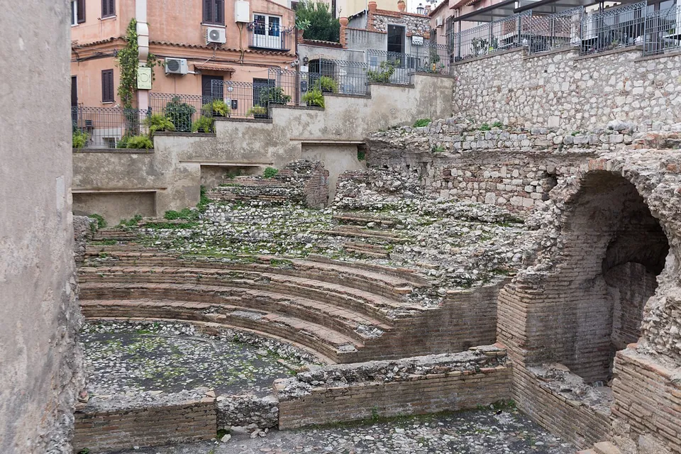A small semicircle of low brick-edged seating rows set in a sunken plot, with a brick vault on one side and apartment buildings rising directly behind it.