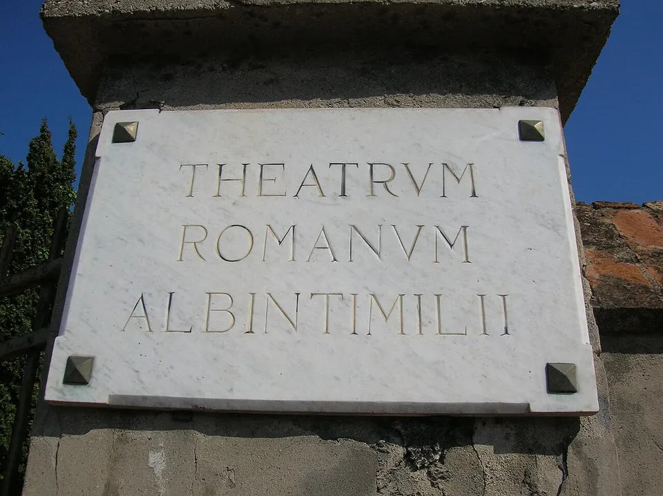 A marble plaque fixed to a pillar, carved in Roman capitals with the words THEATRVM ROMANVM ALBINTIMILII.