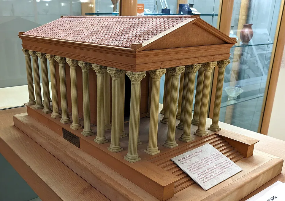 A wooden model of a temple ringed by columns with a tiled roof, set on a stepped base, in a museum display case.