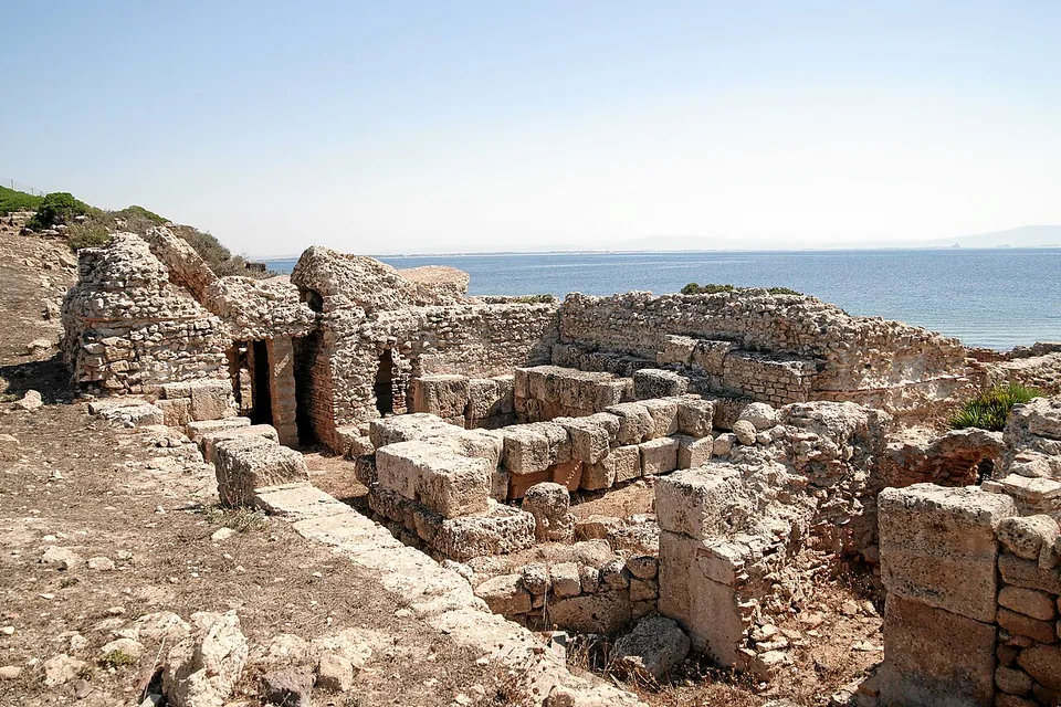 Roofless rooms of a bath building in coursed stone, with doorways and walls standing above head height, on the edge of the sea.