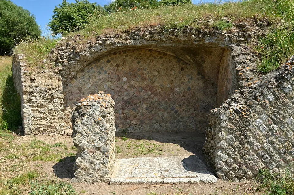 A small vaulted recess built of rough stone, its back wall faced with a net-like pattern of small square stones, with a stone pier standing in front of it on a stone threshold.
