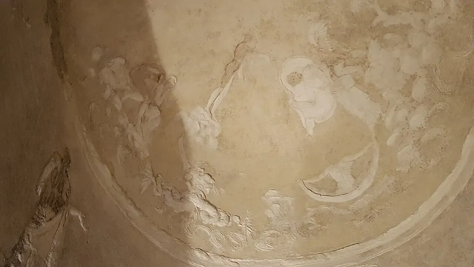 The half-dome of the apse covered in white stucco, with a large circular frame holding figures in relief and smaller figures around its edge.