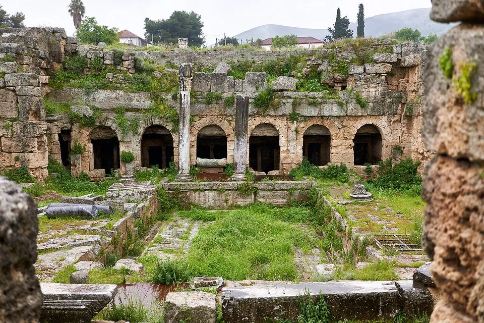 A sunken courtyard with a grassy floor, closed at the back by a two-storey stone facade with a row of round-arched openings and two standing columns.