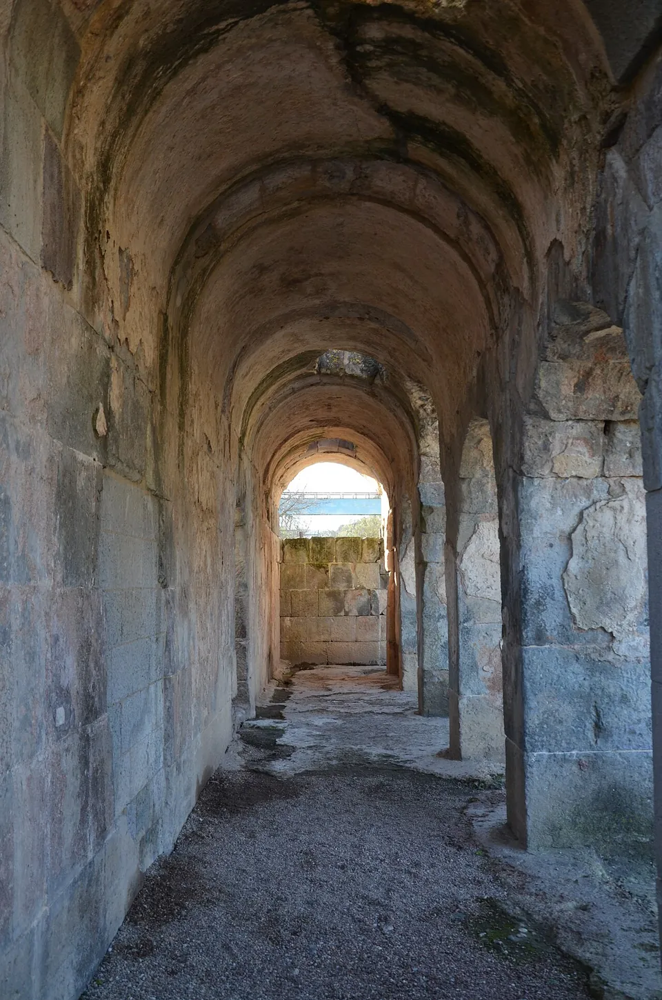 A long barrel-vaulted passage built of large squared stone blocks, with openings along one side and daylight at the far end.