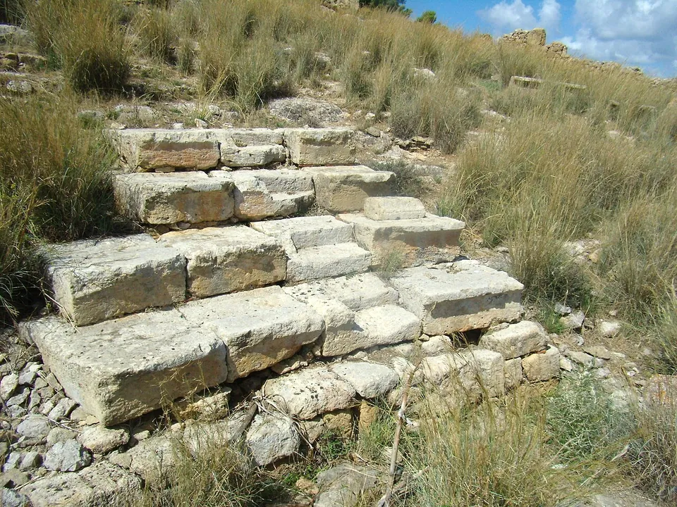 Three rows of large cut stone blocks forming low steps on a grassy, stony slope.