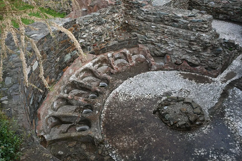 A round room seen from above, its floor of small white stones, ringed by a curved bench of stone and brick with a row of hollow basins set into it.