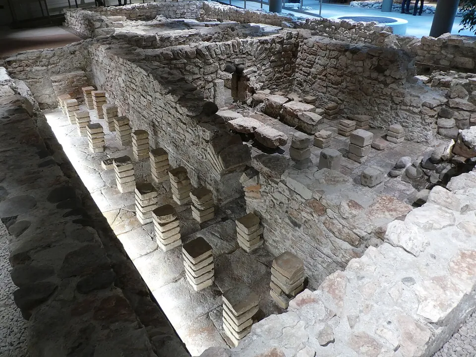 A sunken room lit from below, with rows of short stacks of square tiles standing on its floor between rubble-stone walls.