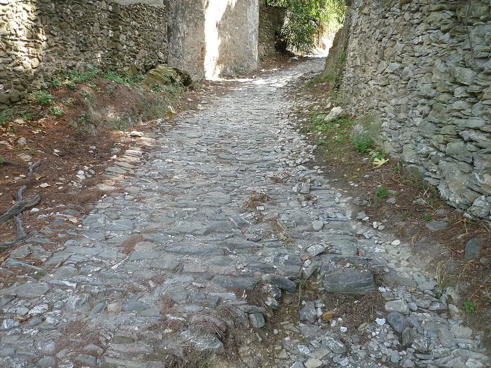 A stony track paved with rough cobbles running between dry-stone walls, with sunlight falling on an opening ahead.
