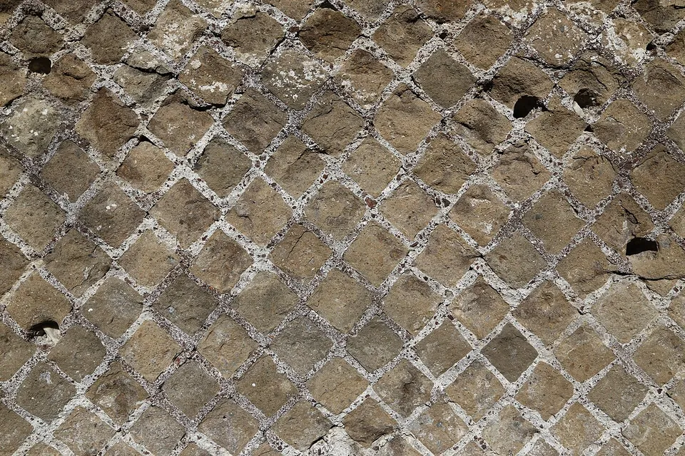 A close view of a wall faced with small square stones set diagonally in a regular net pattern, the mortar between them crumbling.