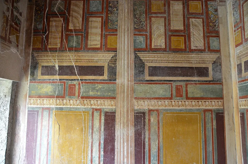 A wall painted to look like a building front, with painted pilasters, a projecting cornice and panels imitating coloured marble in red, green and yellow.