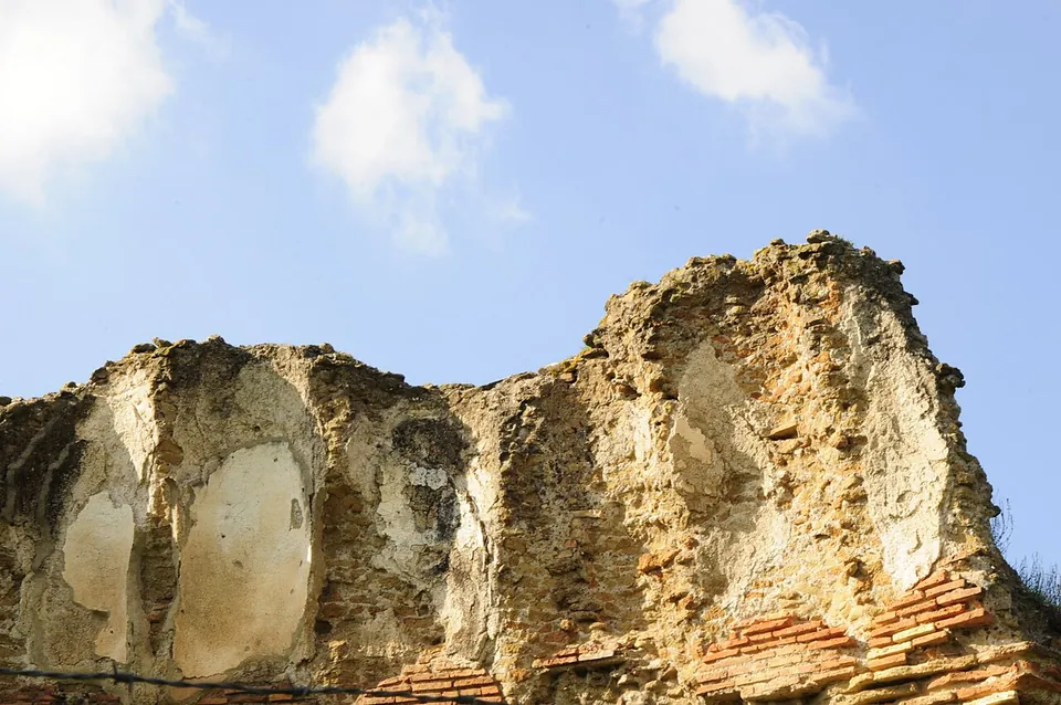 The broken upper edge of a curved vault seen from below, rough concrete with pale patches above a few courses of red brick.