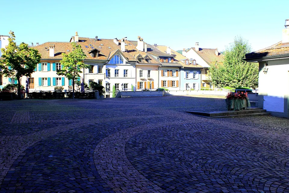 A cobbled square in front of a row of old village houses, with lines of pink paving set into the cobbles.