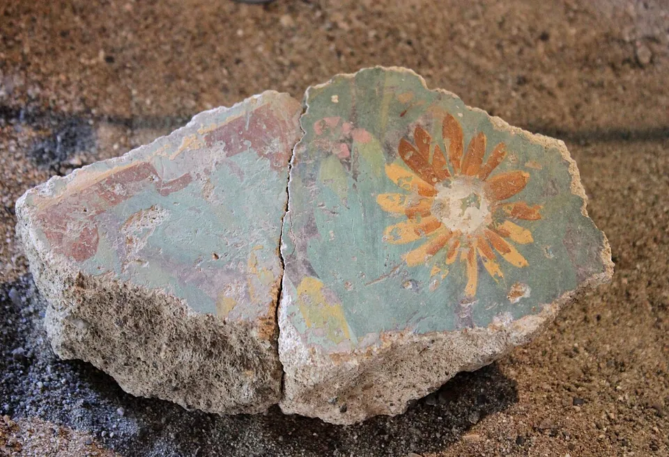 Two joined fragments of painted wall plaster on a gravel bed, one with a reddish band, the other green with an orange and yellow flower.