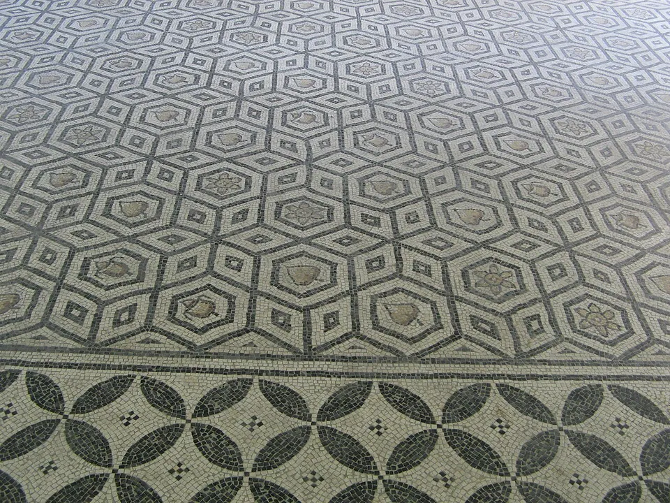A close view of a mosaic of interlocking black hexagons, each enclosing a small flower or leaf, above a border of dark overlapping circles.